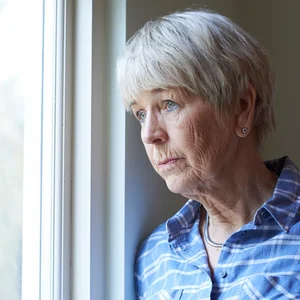 Une femme âgée qui regarde par la fenêtre avec un air triste