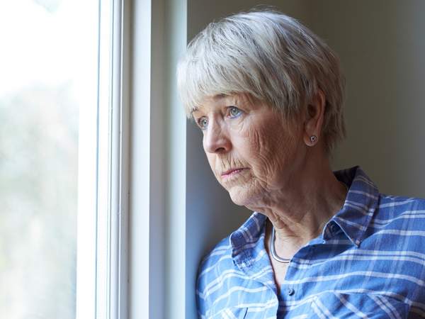 Une femme âgée qui regarde par la fenêtre avec un air triste